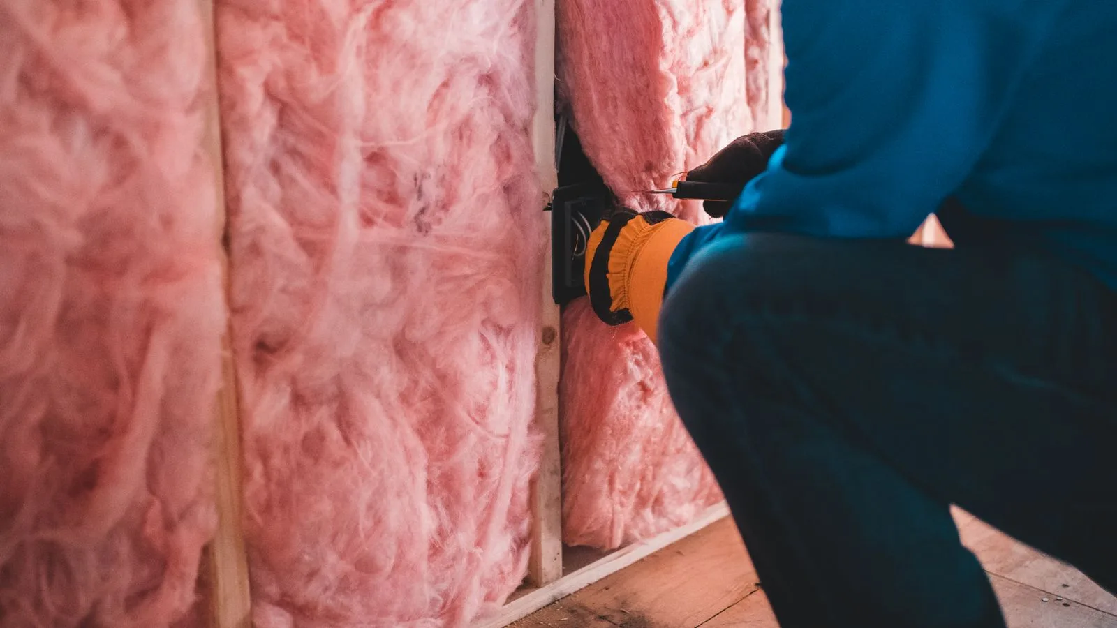 Installer fitting pink fiberglass batt insulation between wall studs